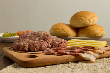 Ingredients for cooking burgers. Raw ground beef meat cutlets on wooden chopping board, cheese, bun,  over wooden background