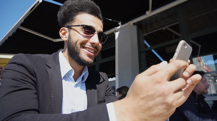 Handsome human clicking on phone s screen and laughing. Attractive guy has short dark hair, beard,...