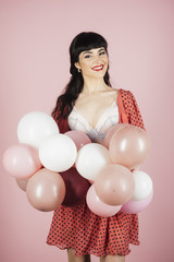 Obraz na płótnie Canvas Sexy woman in white bra holds balloons on pink background.