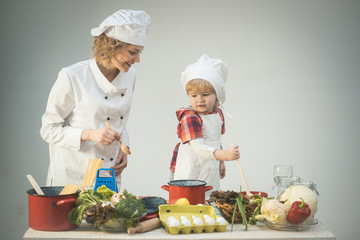 Mother teaches son to cook on light background.