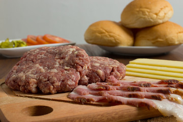 Ingredients for cooking burgers. Raw ground beef meat cutlets on wooden chopping board, cheese, bun,  over wooden background