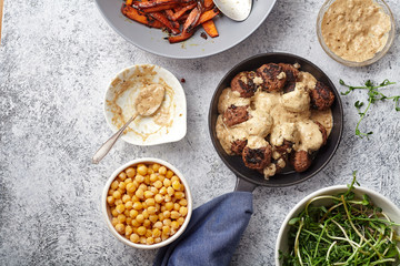 Flatlay with traditional swedish beef meatballs with gravy served in one portion black cast iron pan, handle wrapped in blue towel, plates with sauce, baked carrots and chickpeas. Dinner concept.