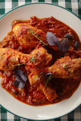 Chicken legs cooked in italian cacciatore style with tomato sauce and fresh basil on green checkered table-cloth