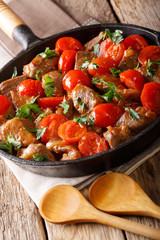 Delicate slowly cooked beef in a sauce with cherry tomatoes and greens close-up in a pan. vertical