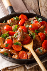 fried beef in hot sauce with cherry tomatoes and greens close-up in pan. vertical