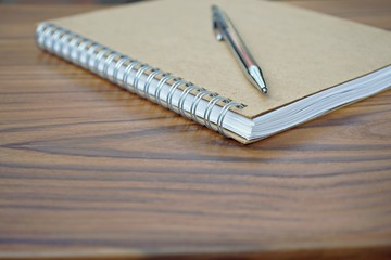 Brown notebook and silver pen with wooden table texture background