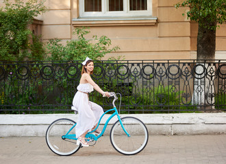 Horizontal shot of a woman in white dress cycling in the city smiling joyfully enjoying warm summer day outdoors travel tourist journey vacation sightseeing.