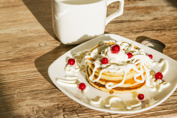 Fresh baked pancakes for Breakfast in a white plate, decorated with sour cream and cranberries, close-up