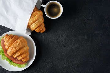Croissant with ham and lettuce, coffee on a dark background. Breakfast flat lay.
