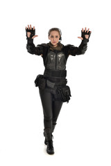 full length portrait of female  soldier wearing black  tactical armour with arms raised, isolated on white studio background.