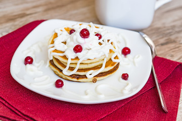Fresh baked pancakes for Breakfast in a white plate, decorated with sour cream and cranberries, close-up