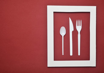Plastic cutlery for picnics in a white frame on a red background. A disposable spoon, fork, knife....