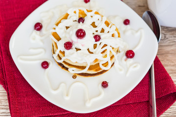 Fresh baked pancakes for Breakfast in a white plate, decorated with sour cream and cranberries, close-up