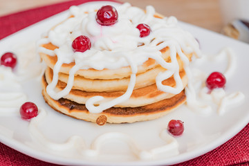 Fresh baked pancakes for Breakfast in a white plate, decorated with sour cream and cranberries, close-up