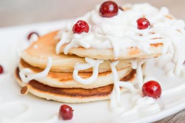 Fresh baked pancakes for Breakfast in a white plate, decorated with sour cream and cranberries, close-up