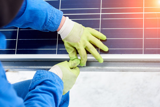 Technician in blue suit installing blue solar panels with screw. Photovoltaic modules as renewable energy source. Alternative energy production innovation ecological sustainable resources