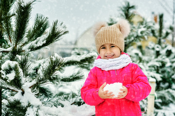 Portrait of a girl in winter outdoors. The child plays with the snow.