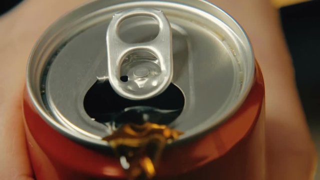 Coca-Cola is poured from a can of red color against a dark background. Slow-motion close-up shooting