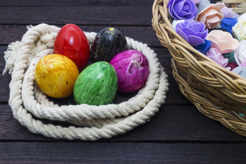 Easter holiday concept. Easter eggs in rope and basket with paper flowers on wood