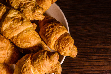 Plate with fresh croissants on a dark wooden table. Top view