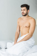 handsome bearded shirtless man sitting on white bed