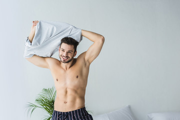 Obraz premium handsome sexy smiling man taking off his t-shirt in bedroom