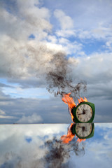 Burning old clock on mirror on sky background, end of time