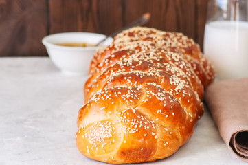 Homemade sesame seeds challah bread, glass of milk and orange jam  on a white background.