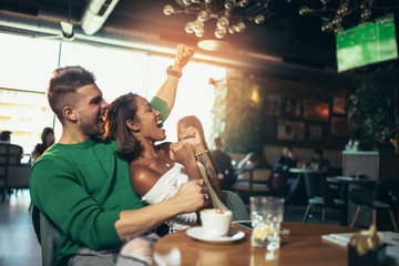 Modern couple in cafe looking excited and happy after their favorite football team scored a touchdown. Selective focus