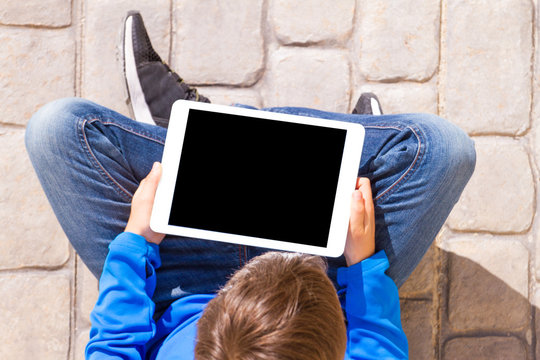 Tablet computer in the hands of a child who sitting on the ground.