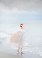 Fototapeta na wymiar Bride holds her dress up standing in the sea water on the beach