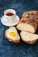 Homemade sesame seeds challah bread on a wire rack and a cup of red tea on a blue stone background.