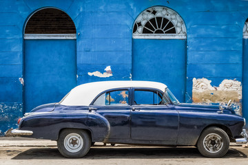 Blauer amerikanischer Oldtimer mit weissem Dach parkt vor einem historischen Gebäude in Havanna...