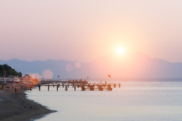 Dawn on the sea beach. Pier. The mountains in the morning mist are far away.