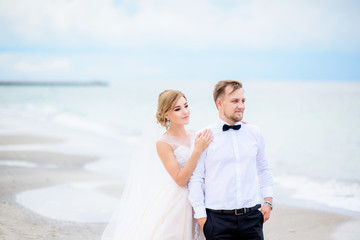 Bride stands behind groom facing the wind on beach