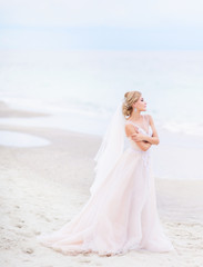 Fototapeta na wymiar Bride looks gorgeous standing on the white sand before the sea