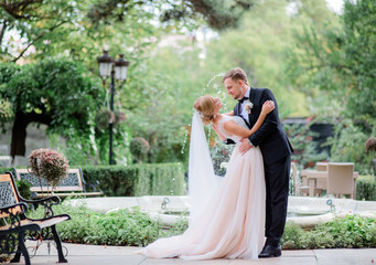 Adorable newlyweds hug each other tender posing before a fountain in the garden