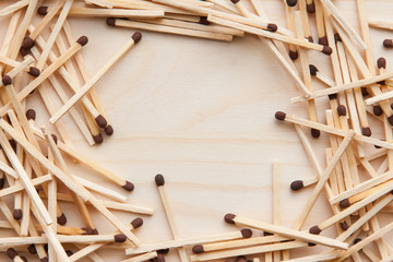 wooden unburned matches with black heads scattered against a light brown wood. empty space in the center