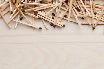 wooden unburned matches with black heads scattered against a light brown wood. empty space from below