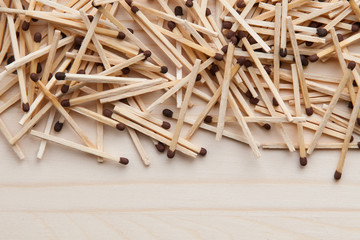 wooden unburned matches with black heads scattered against a light brown wood. empty space from below