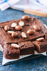Dark chocolate brownie square on a wire rack decorated with creamy chocolate eggs. Blue stone background.