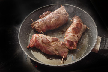 beef roulades, german stuffed meat rolls roast in a pan on the black stove, copy space