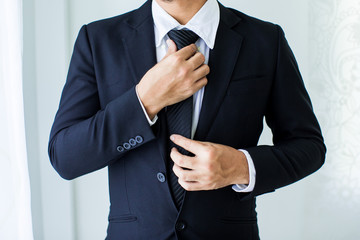 People, business,fashion and clothing concept - close up of man in shirt dressing up and adjusting tie on neck at home. - obrazy, fototapety, plakaty