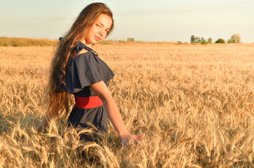 A young woman stands among the wheat fields under the sun