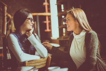Two young girls sitting in cafe and having conversation.