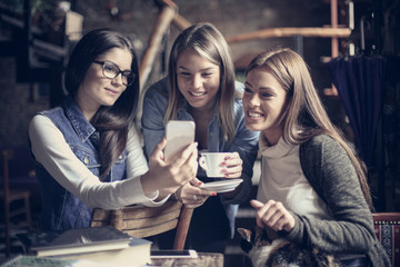 Three young students enjoying in cafe and using smart phone together.