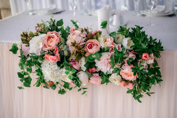 Garland of white and pink roses and hydrangeas lies on the dinner table for newlyweds