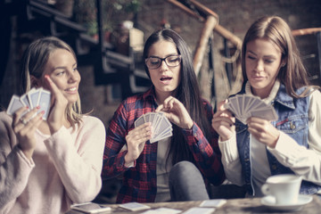 Three girls in cafe playing game cards.