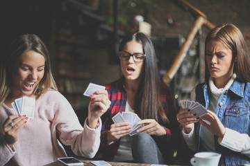 Three best friends in cafe playing together game cards.