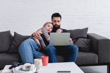 tattooed couple hugging and watching movie together at home